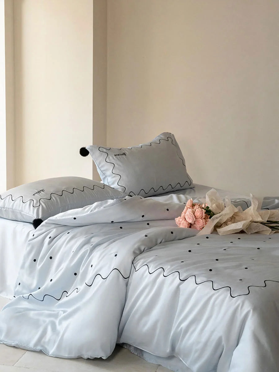 Angled shot of the Baby Blue & Black embroidered Tencel bedding, showing its silky sheen. - RoomDen