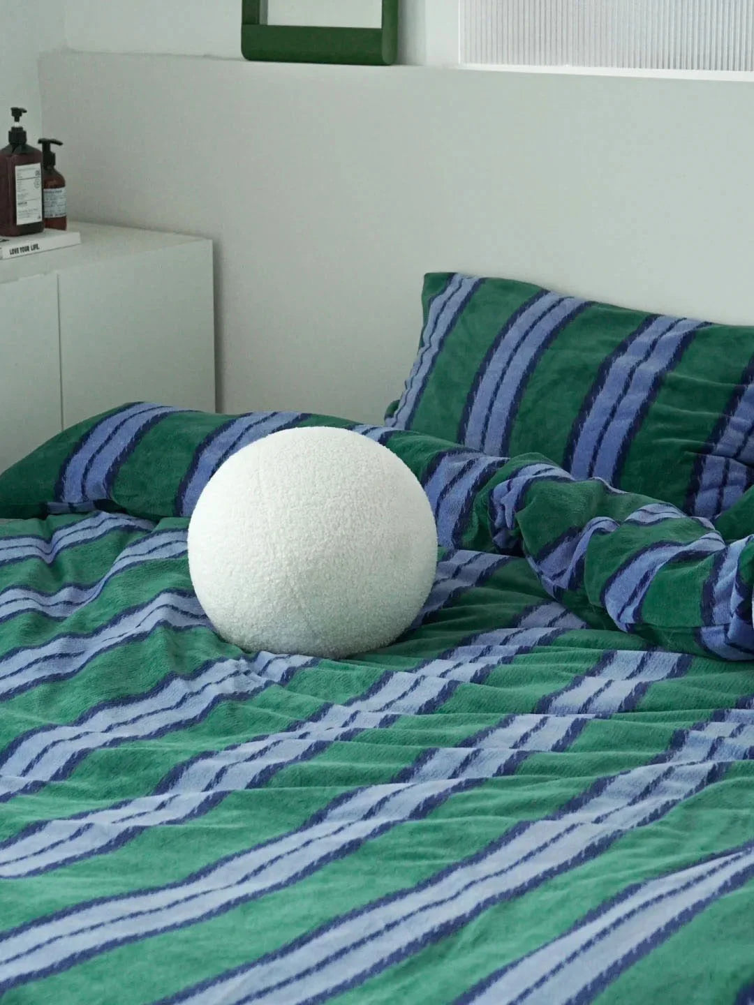 The green and blue striped velvet bedding set styled with a white spherical bouclé pillow - RoomDen.