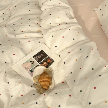 A lifestyle shot of the white polka dot bedding set styled with a magazine and a croissant on a plate. - RoomDen