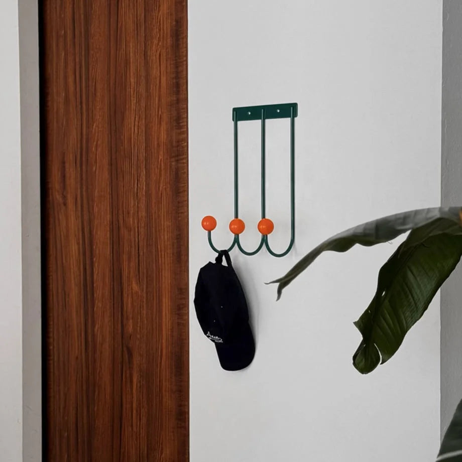 Lifestyle image showing the Green & Orange wall hooks next to a doorway and a large plant. - RoomDen