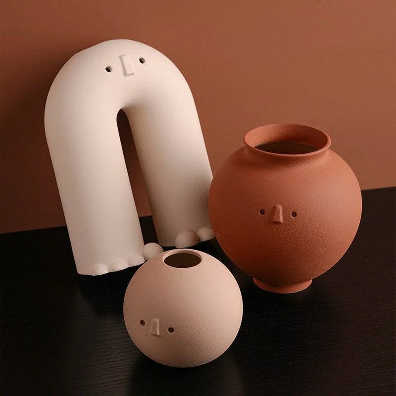 The full set of three Frosted Minimalist Face Vases (Arch, Pot, Ball) arranged on a dark surface against a brown wall. - RoomDen