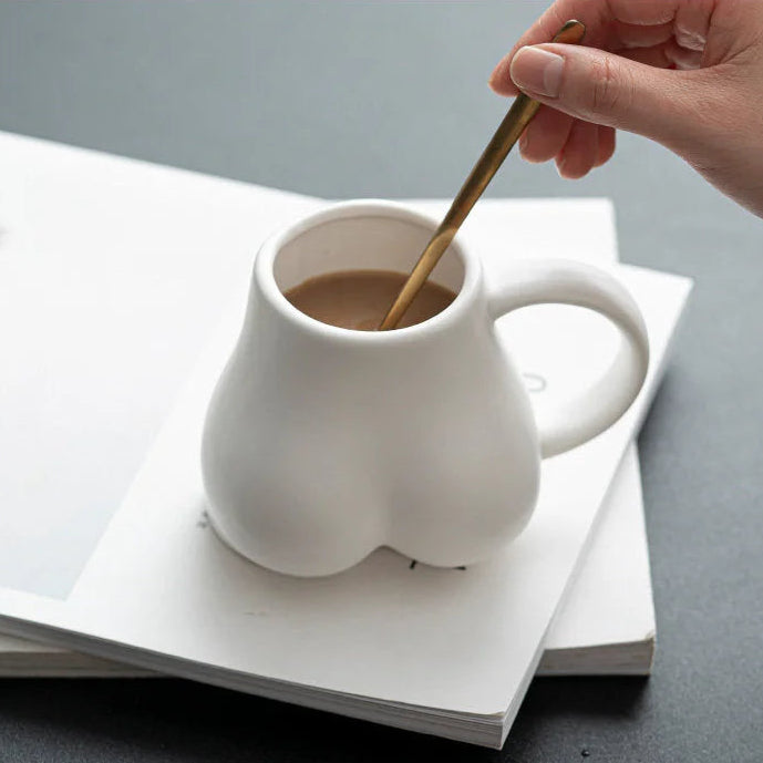 A hand stirring a coffee in the white sculptural body ceramic mug with a golden spoon. - RoomDen