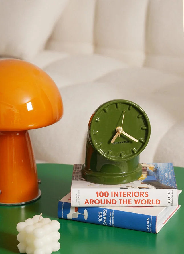Lifestyle image of the olive green Industrial Pipe Ceramic Table Clock sitting on a stack of books next to an orange mushroom lamp - RoomDen