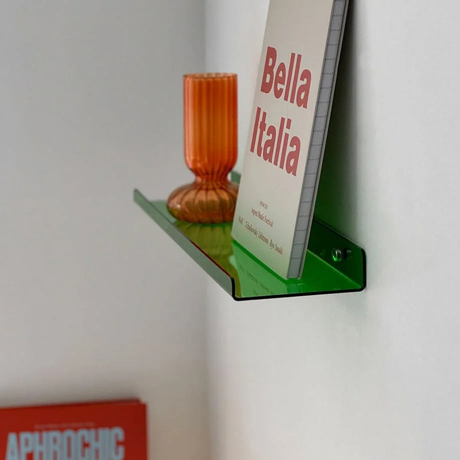 The Sleek Minimalist Acrylic Floating Shelf in a bright green color variant, holding a book and an orange textured vase.