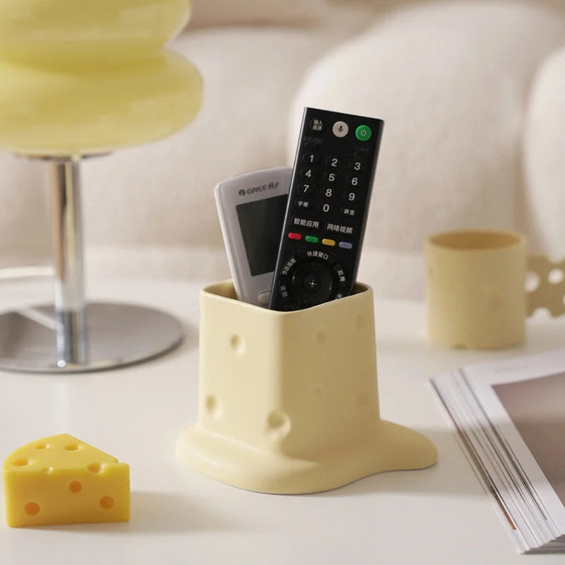 A beige melting cheese ceramic organizer holding two remote controls on a white desk. - RoomDen