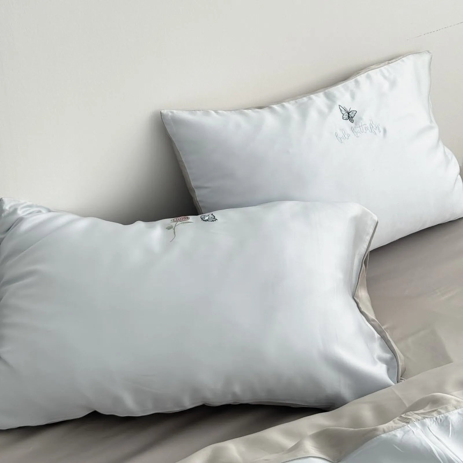 Two Cloud Blue pillowcases from the embroidered Tencel bedding set, showing the smooth texture and subtle grey piping detail.