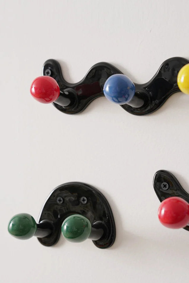 Close-up of installed black ceramic wall hooks with multicolor balls on a white wall.