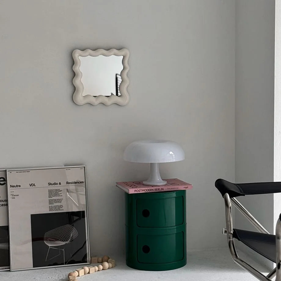 Off-white wavy mirror on a wall above a green storage cart and a mushroom lamp - RoomDen