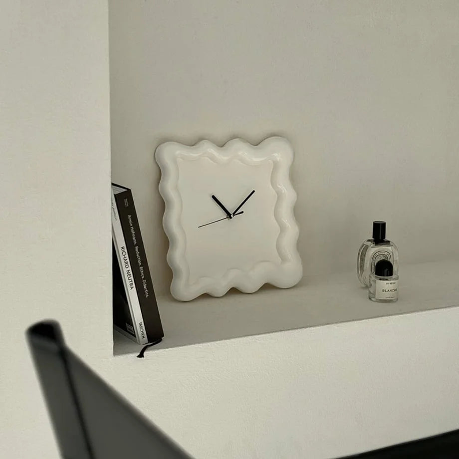 Front view of the off-white Wavy Squiggle Clock in a minimalist shelf setting. - RoomDen