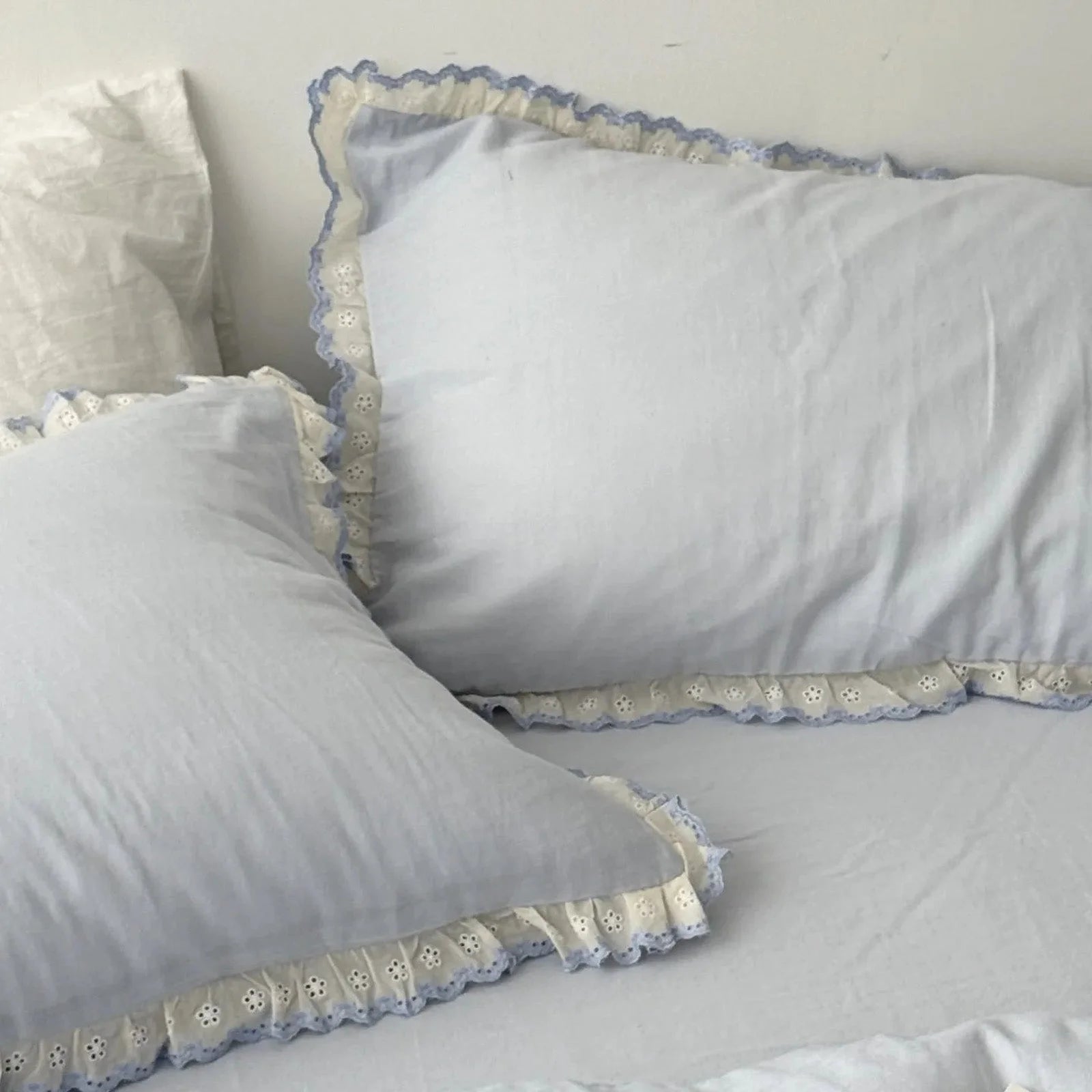 Close-up on two sky blue pillowcases with detailed white and blue embroidered lace ruffle trim.