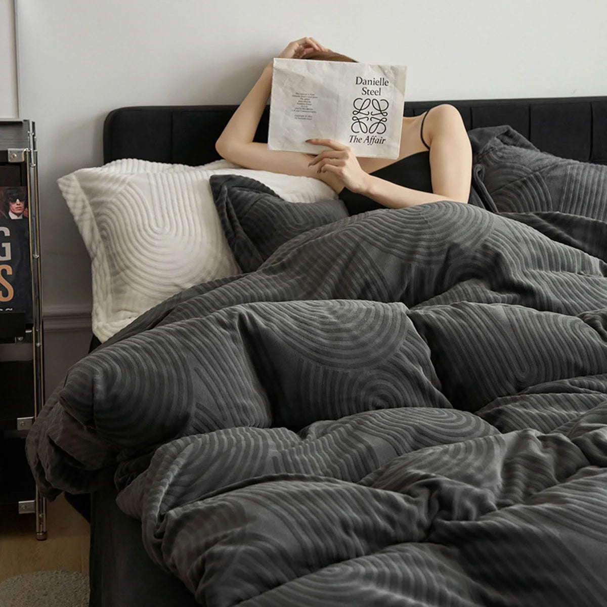 Woman holding a book in bed, wrapped in the plush Charcoal Grey Wavy Arch Flannel Fleece Bedding Set. - RoomDen