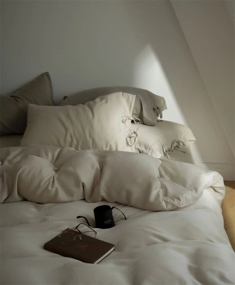 The Oatmeal Beige Tencel Bedding Set looking soft and inviting, with a book and glasses on top - RoomDen
