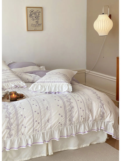 Angled shot of the Lavender embroidered bedding set, showing the ruffles and a candle on the bed.