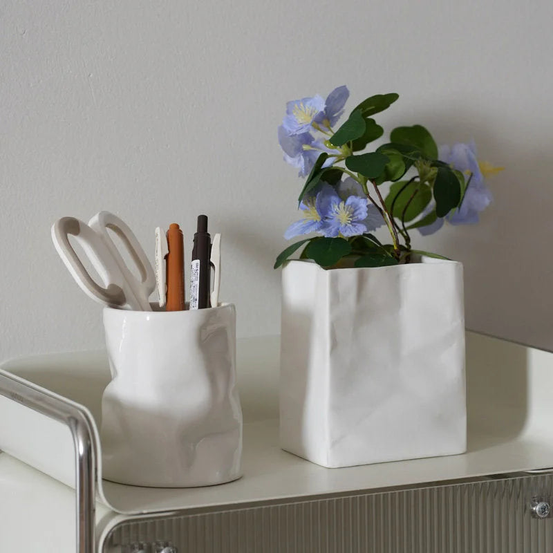 A white crumpled ceramic organizer holding pens and another used as a vase for purple flowers on a white cart. - RoomDen