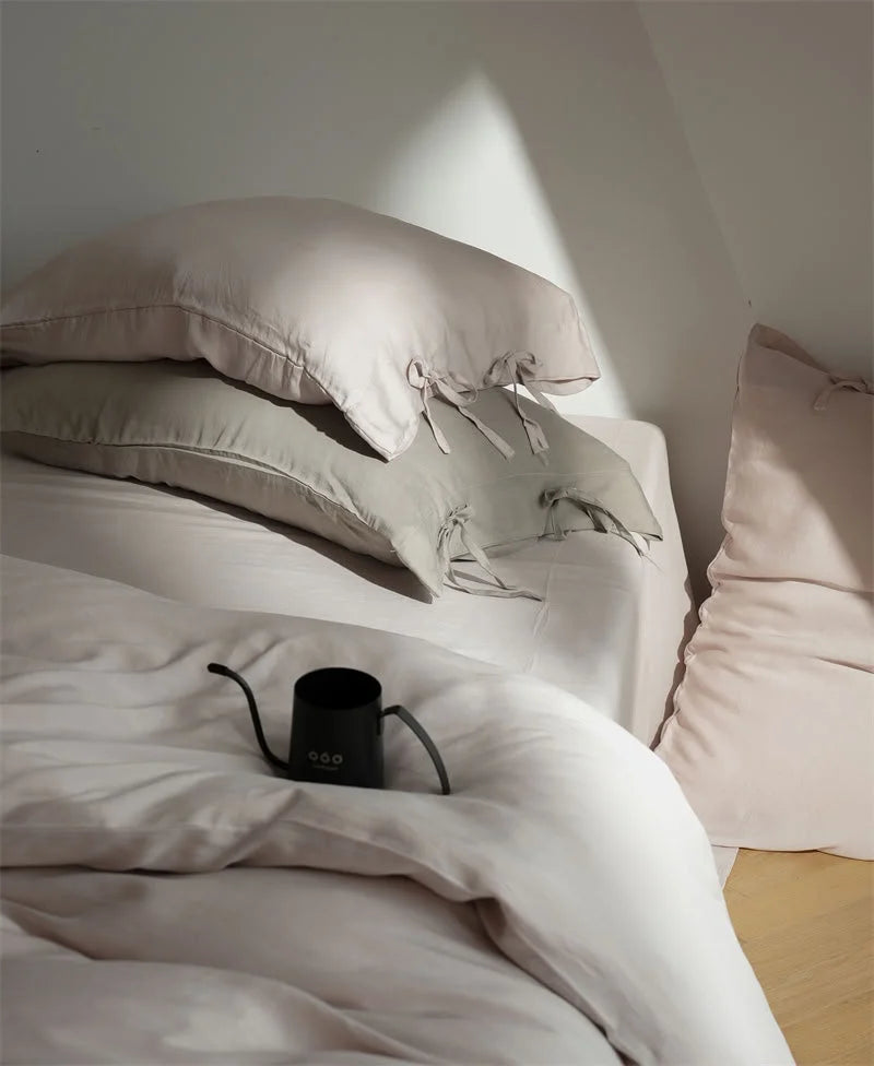 Close-up of the tie-closure pillowcases in Dusty Rose, with a black pour-over kettle on the bed - RoomDen