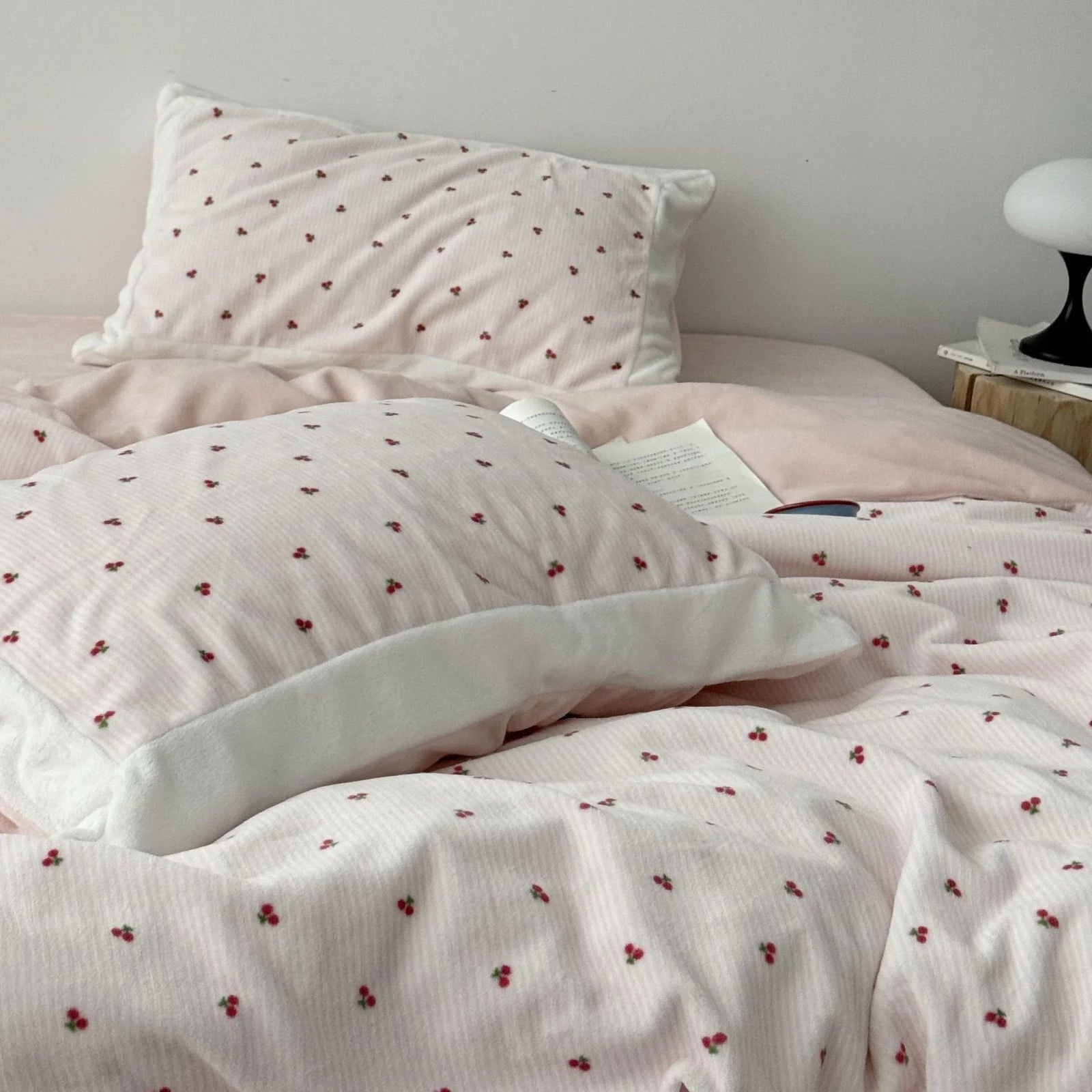 A fluffy pillow with a cherry pattern resting on a solid pink fleece sheet, part of a bedding set. - RoomDen
