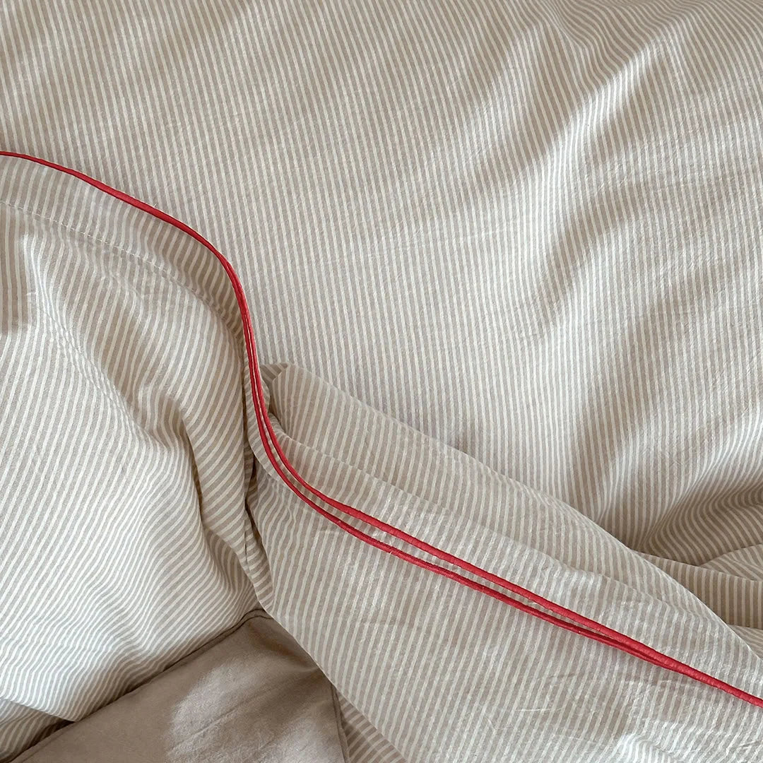 Macro shot showing the texture of the beige pinstripe fabric and the red corded edge.