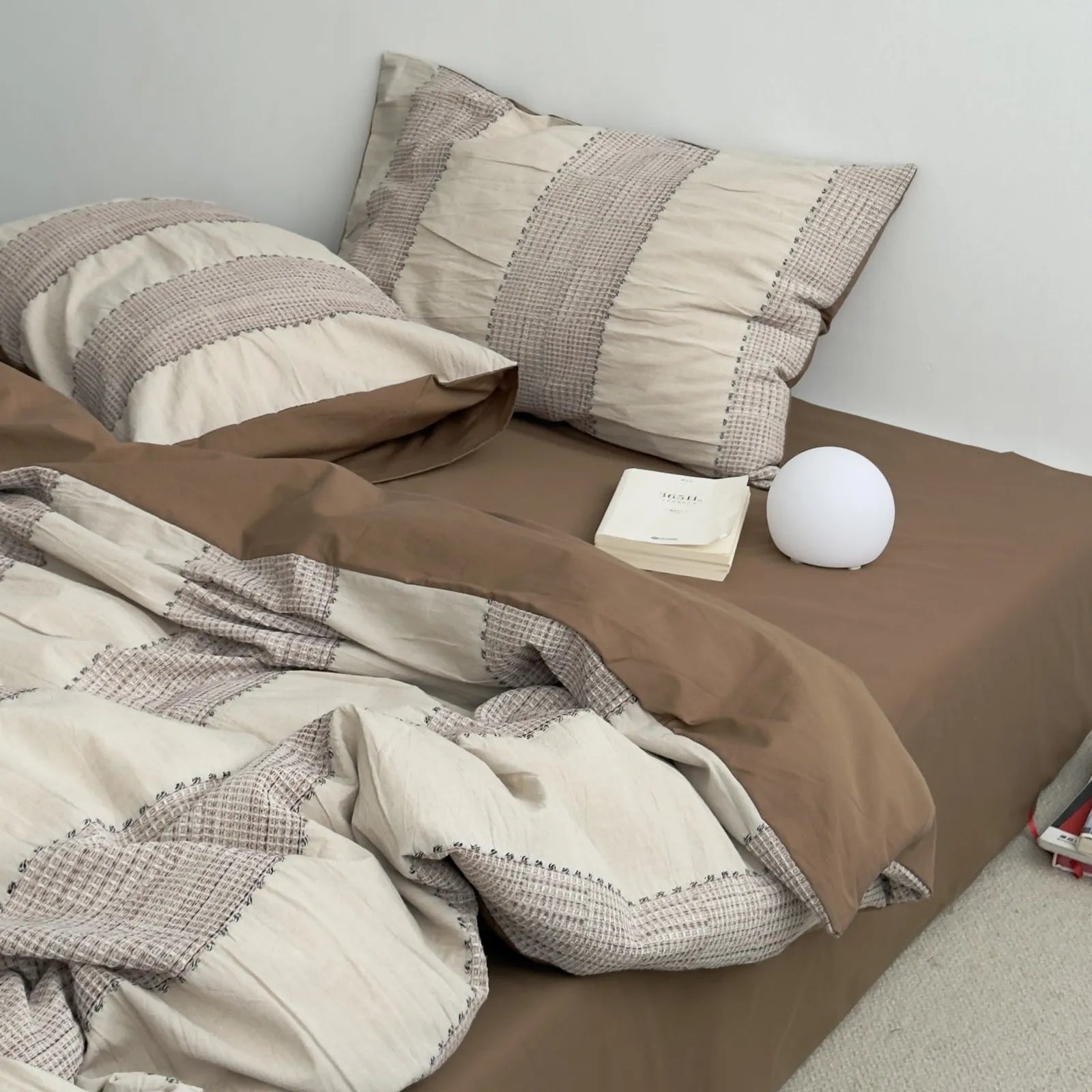 The Mocha Brown woven stripe bedding set styled with a bedside lamp and book in a cozy setting.