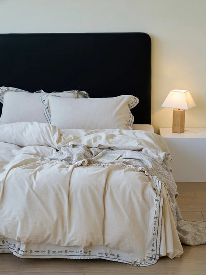 Full view of a bed with Textured Embroidered Ruffle Linen Bedding Set, featuring a black headboard and a bedside lamp - RoomDen.