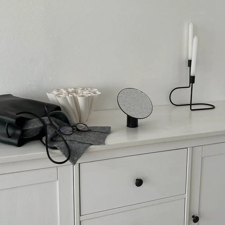 The black rotating desktop mirror in a minimalist room setting with a candle holder.