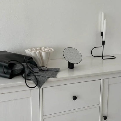 The black rotating desktop mirror in a minimalist room setting with a candle holder.