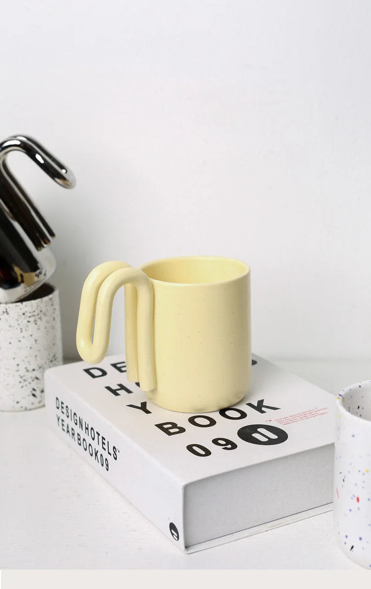 Butter Yellow loop handle ceramic mug resting on a white design book - RoomDen
