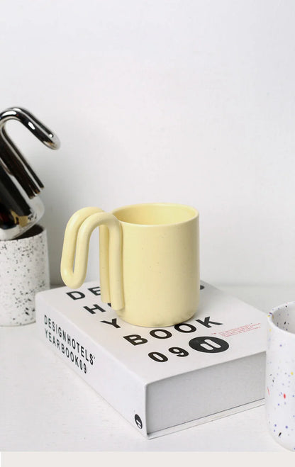 Butter Yellow loop handle ceramic mug resting on a white design book - RoomDen