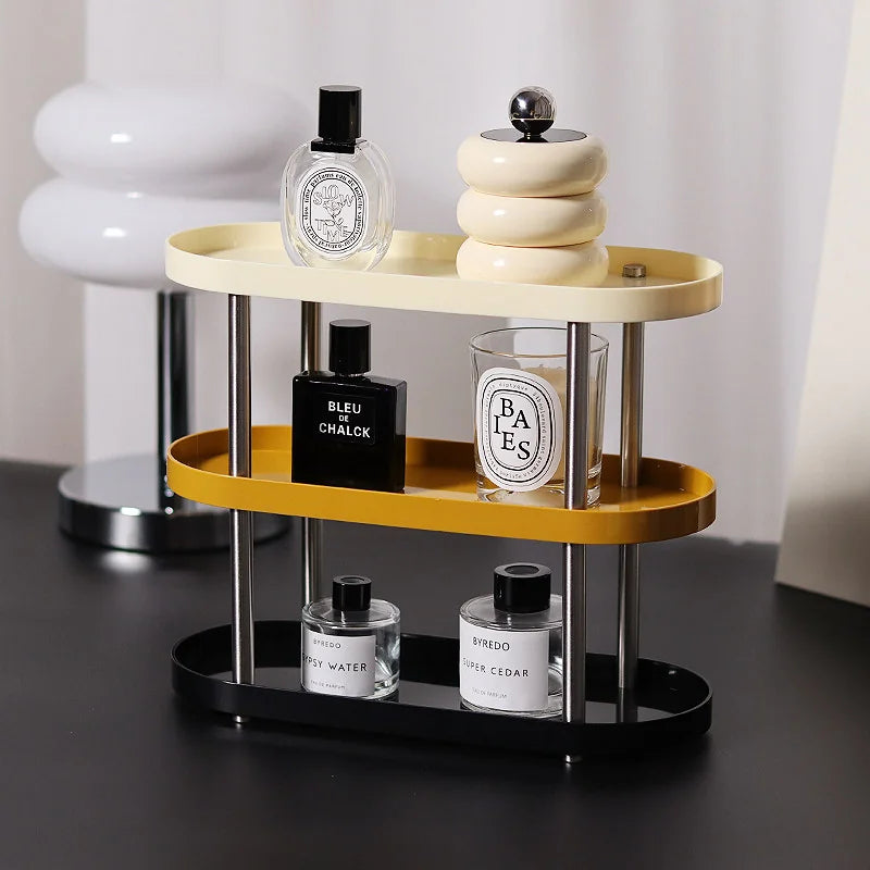 The three-tier tricolor makeup organizer holding perfume bottles and a candle on a desk. - RoomDen