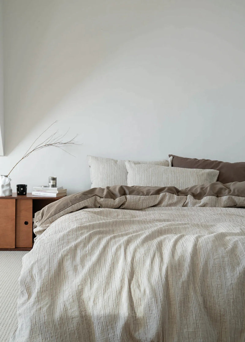 Textured Pinstripe Washed Cotton Bedding Set in Latte Brown in a bright minimalist bedroom, the warm tone hiding the wrinkle shadows. — RoomDen
