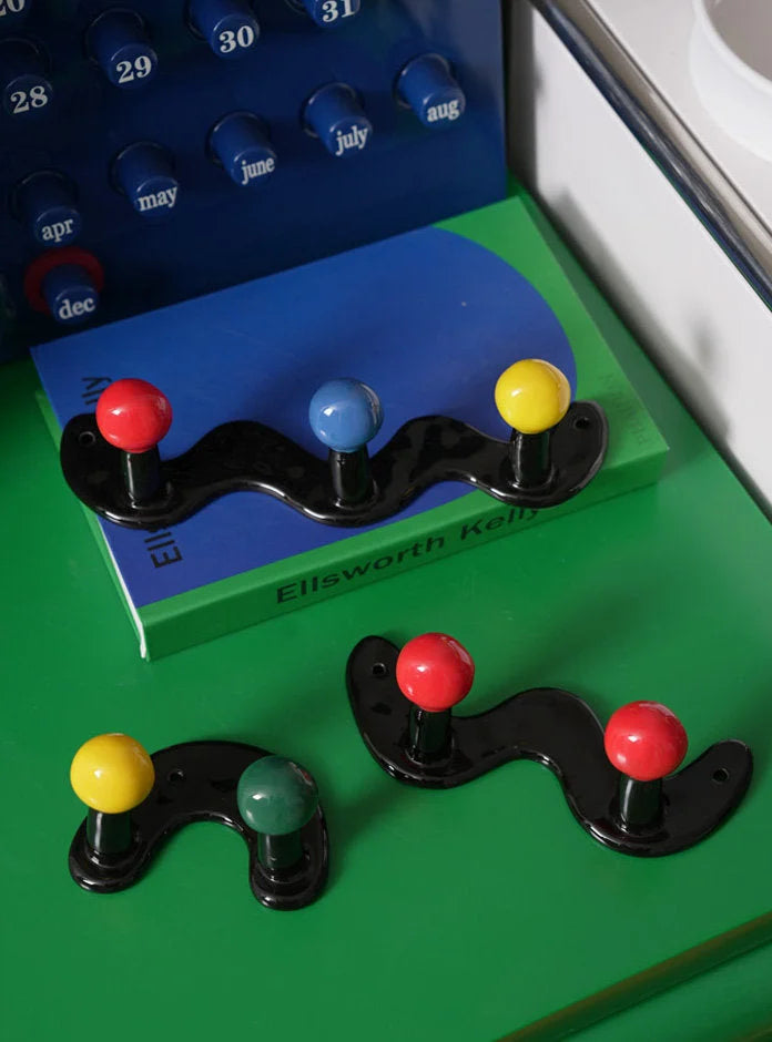 Several colorful wavy and U-shaped ceramic hooks displayed on a green surface next to a blue calendar.