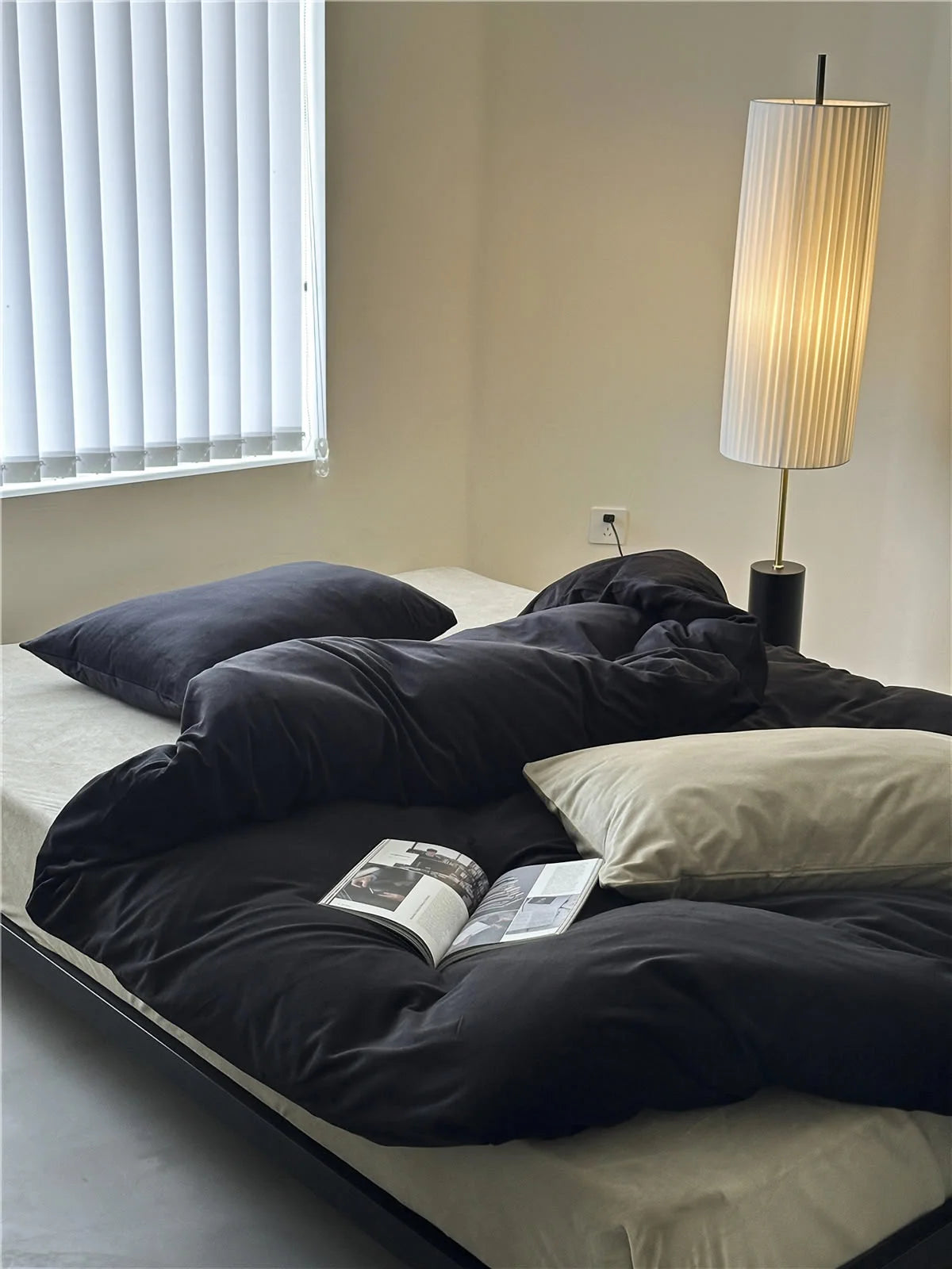 A neatly made bed featuring the Obsidian Black velvet duvet cover and a cream pillow, with an open book. - RoomDen