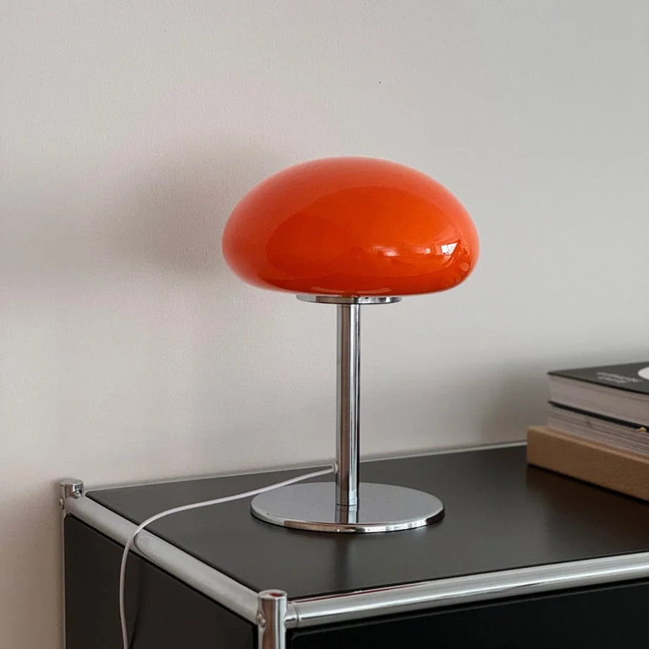The orange mushroom lamp with its chrome metal base on a black surface - RoomDen.