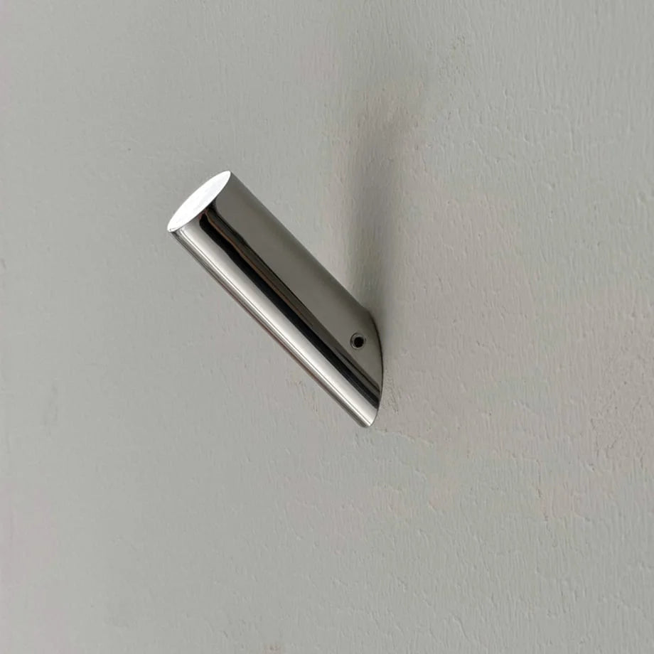 Close-up detail of the cylindrical metal wall hook mounted on a white wall, showing the set screw. - RoomDen