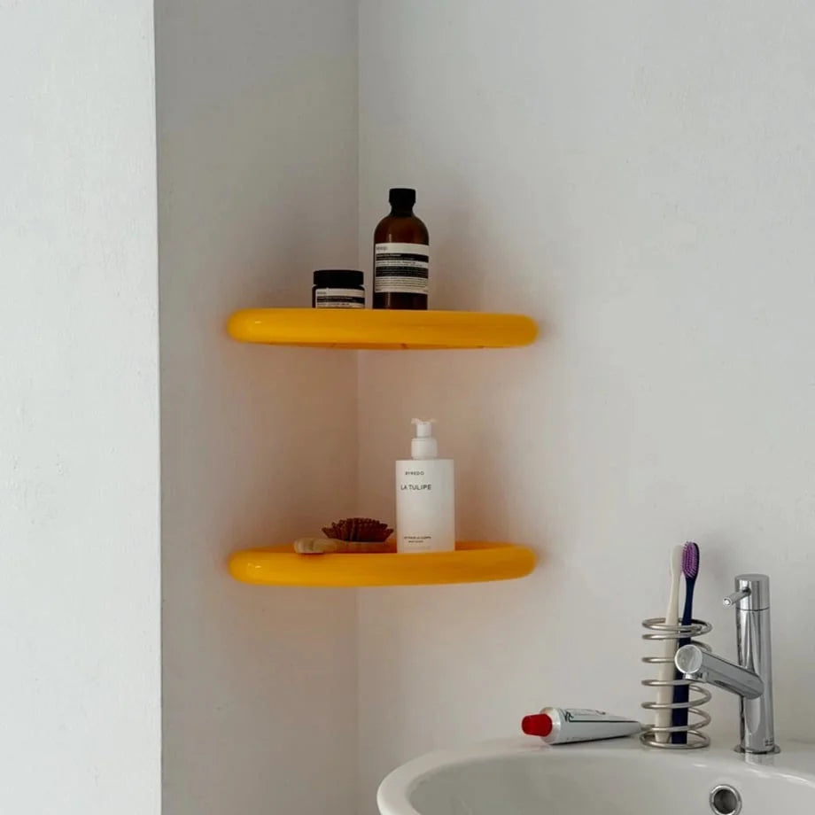 Two yellow Chunky Curved Corner Shelves installed in a white bathroom corner, holding toiletries and skincare. - RoomDen