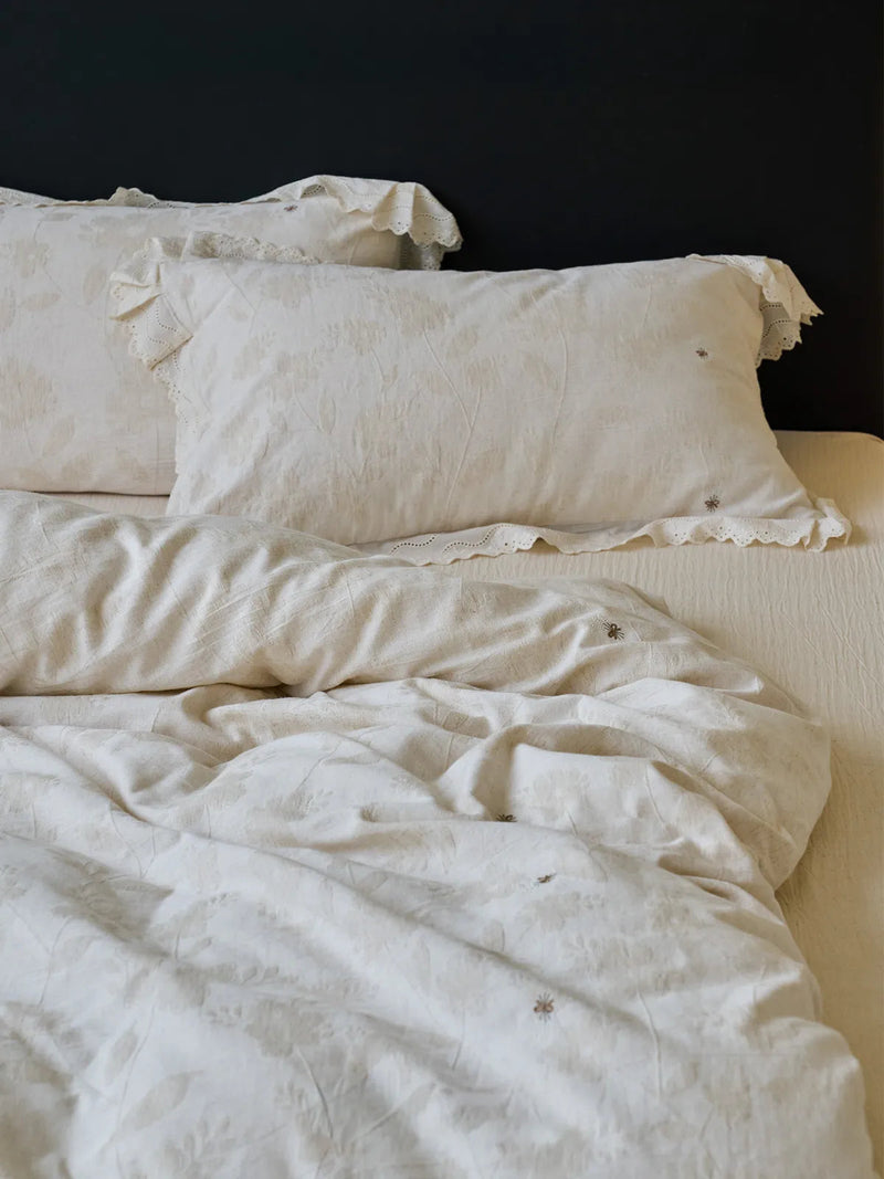 Antique white linen bedding set with ruffle lace pillowcases against a dark headboard — RoomDen