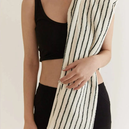 A woman in workout gear holding a folded white and black striped face towel.
