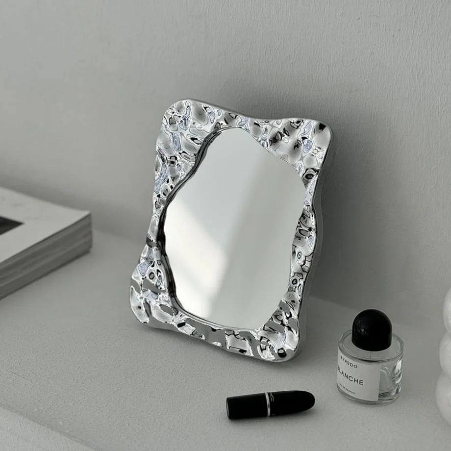 Lifestyle scene featuring the wavy chrome vanity mirror as a decorative art piece on a modern shelf - RoomDen