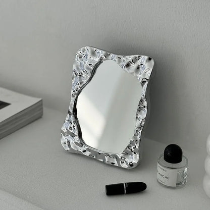 Lifestyle scene featuring the wavy chrome vanity mirror as a decorative art piece on a modern shelf - RoomDen