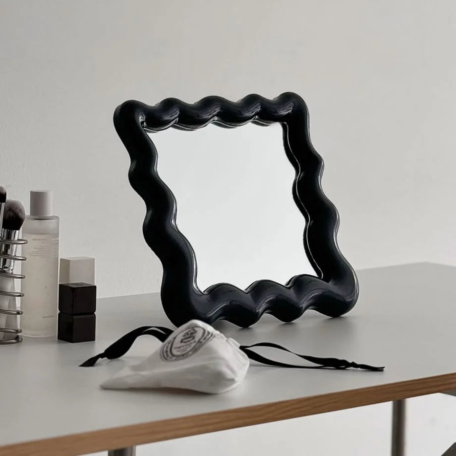 Angled view of the black squiggle mirror on a desk, reflecting the room - RoomDen