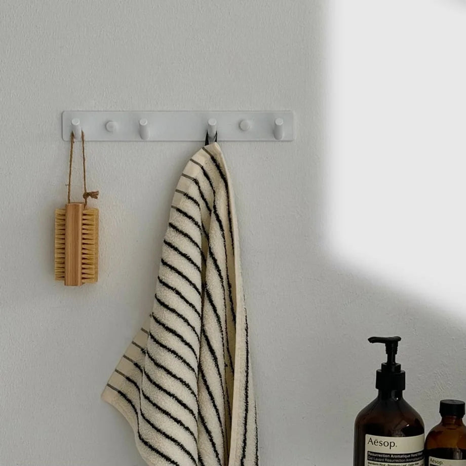 White minimalist metal wall hooks installed in a bathroom, holding a striped towel and a body brush - RoomDen.