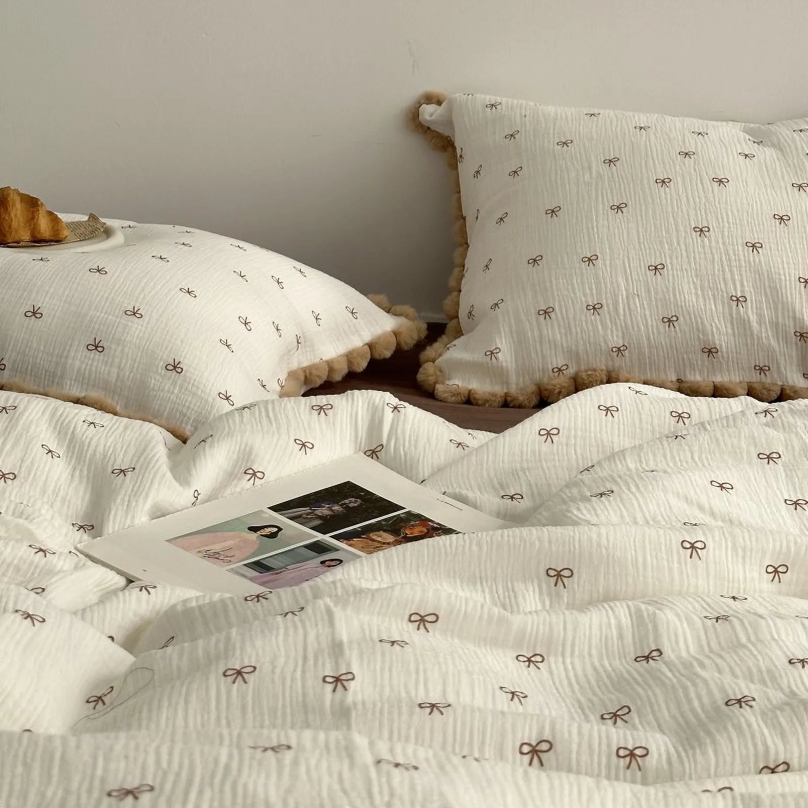 Detailed shot of the crinkled washed cotton fabric of the bow print duvet cover with a magazine resting on it. - RoomDen