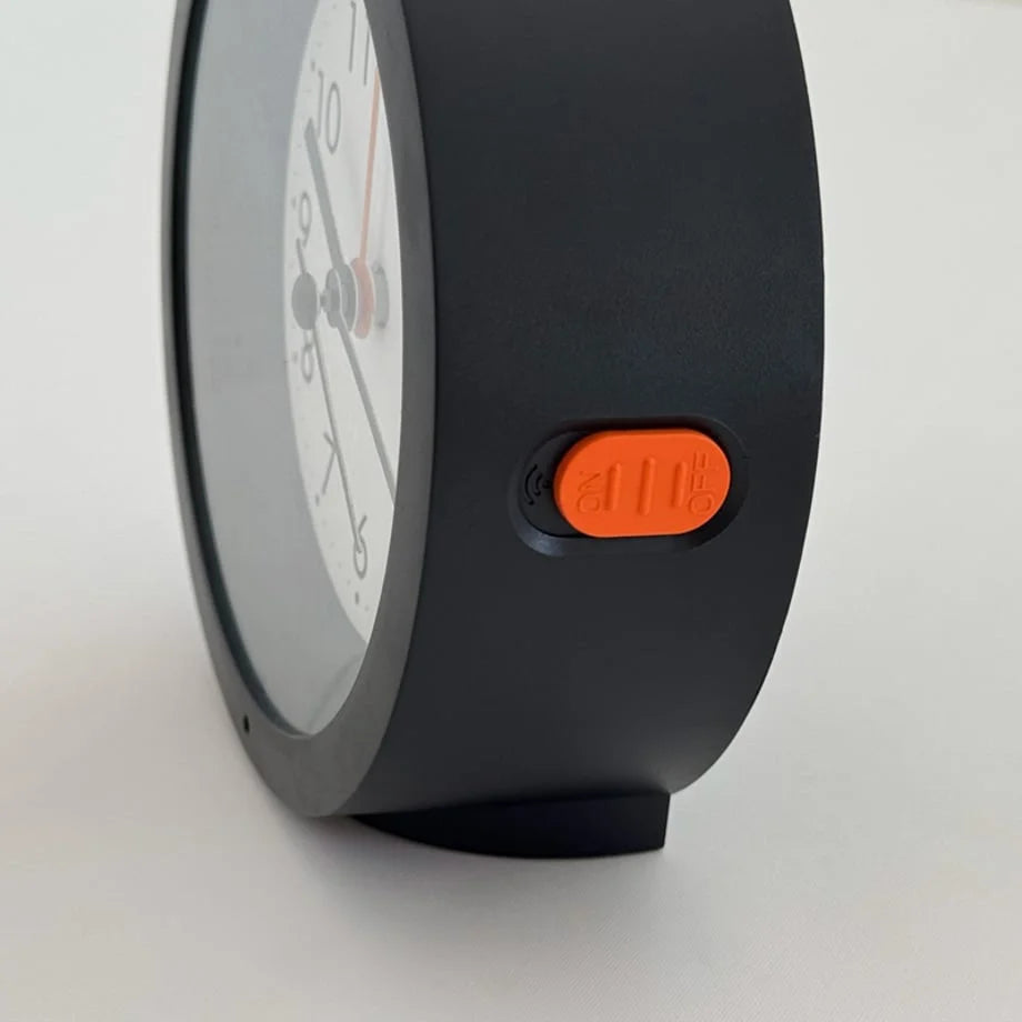 Close-up of the orange alarm switch on the side of the black Minimalist Matte Analog Alarm Clock. - RoomDen