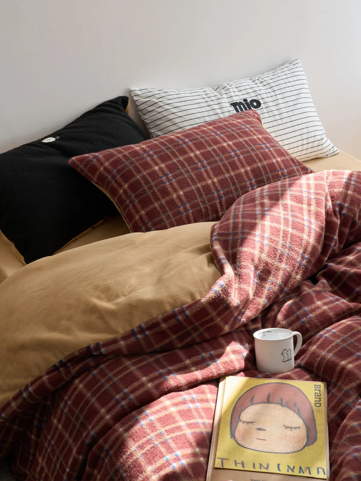 Close-up of a red plaid flannel fleece duvet cover on a bed, styled with a black pillow, a striped pillow, and a book. - RoomDen