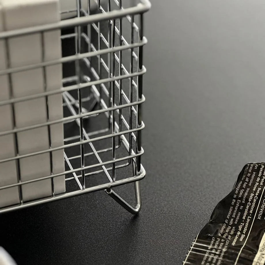 Detail shot of the metal grid organizer's welded joints and raised wire feet on a black surface - RoomDen.