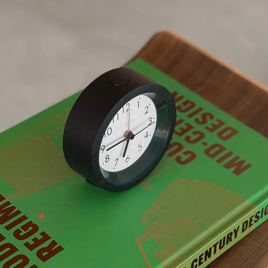 Angled view of the black analog alarm clock showing the top snooze/light button. - RoomDen