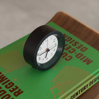 Angled view of the black analog alarm clock showing the top snooze/light button. - RoomDen