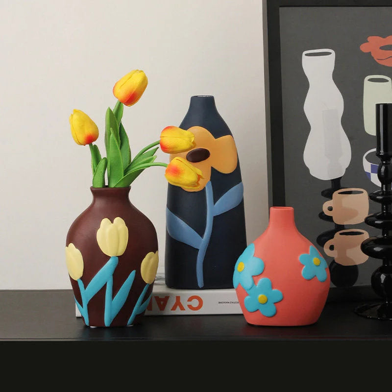 Three Pop Art Floral Ceramic Vases in brown, navy, and coral, displayed on a black shelf with yellow tulips. - RoomDen