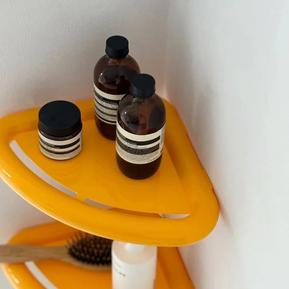 Close-up on the yellow Chunky Curved Corner Shelf holding Aesop skincare products, showing its storage capacity. - RoomDen