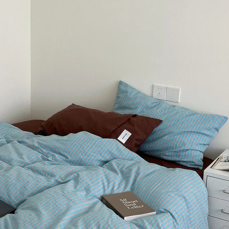 A cozy corner featuring the Blue & Brown Striped bedding with a book titled "All About Soul Letter" on the duvet - RoomDen.
