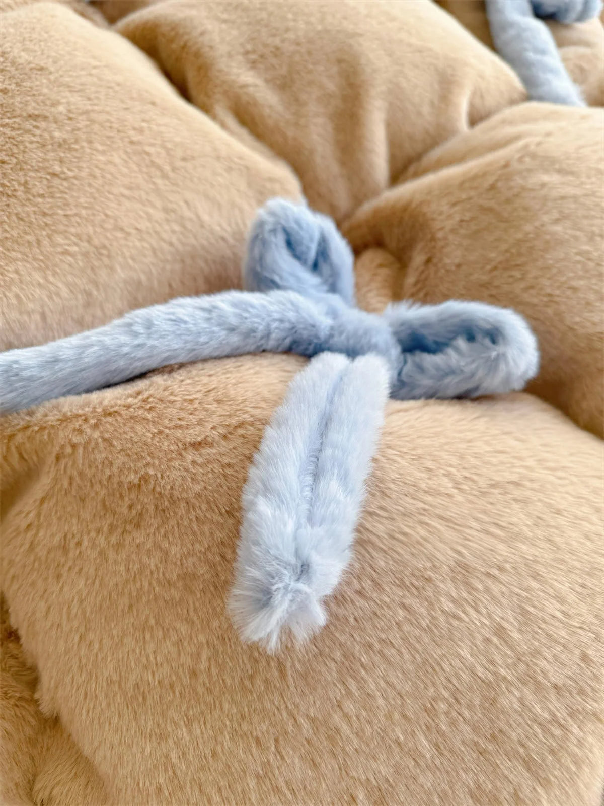 Close-up detail of a blue plush bowknot on the khaki brown fleece comforter.
